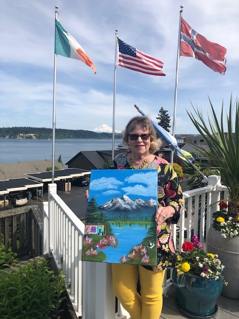 Anna's friend Robin with her son Aaron's painting of The Three Sisters Mountains with quilts displayed